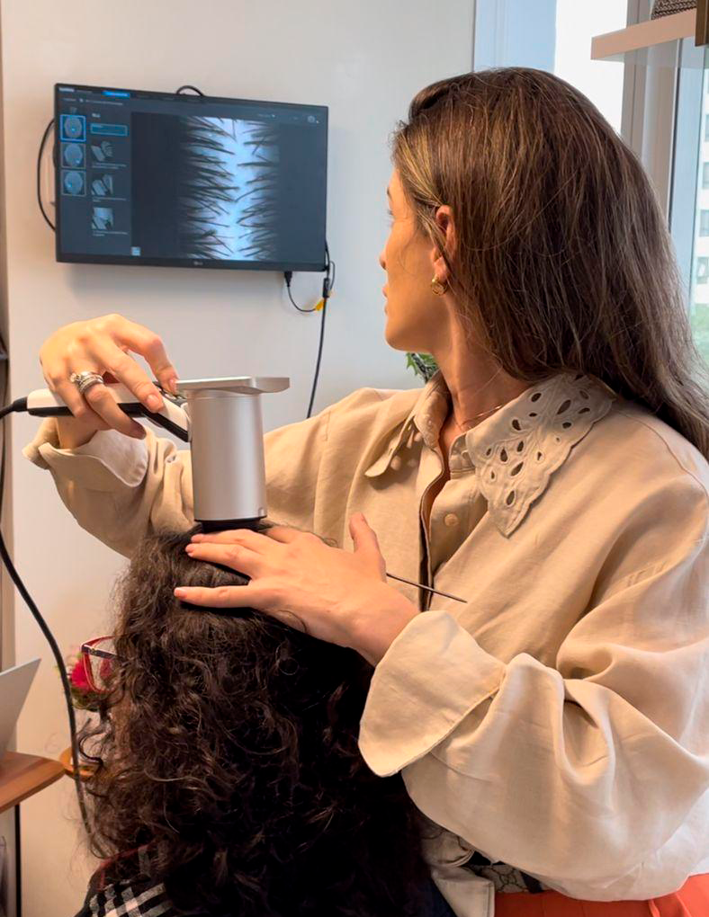 Imagem de uma mulher sentada na cadeira fazendo a medição de folículos saudáveis para a possível extração com o Hair Metrix